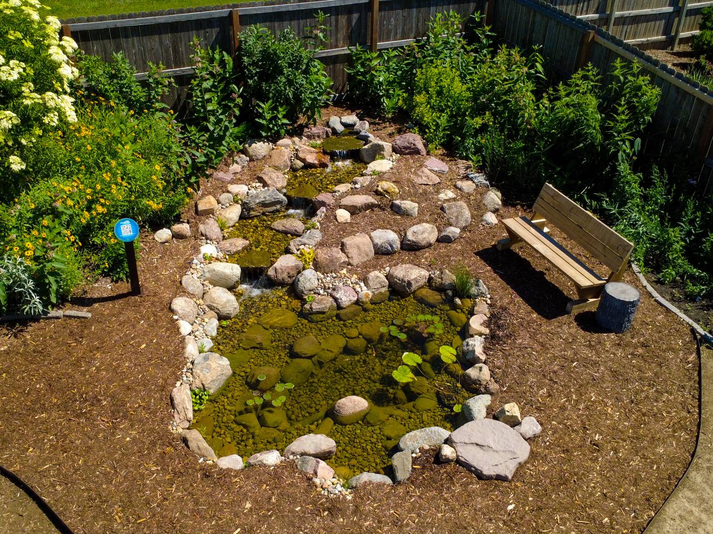 Backyard pond and stepped stream edged with boulders and river rock next to a garden bench