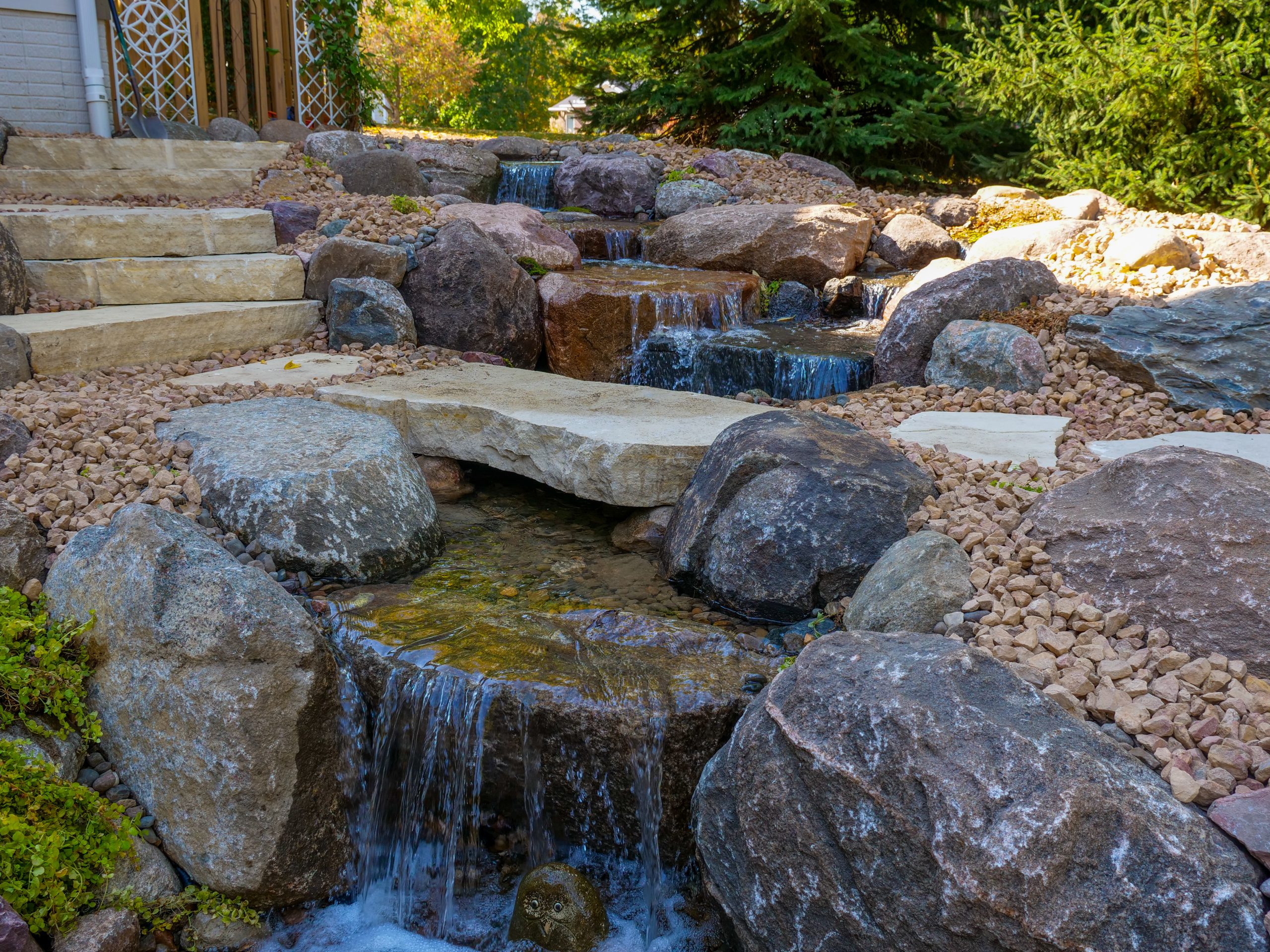 Award-winning pondless waterfall in Ankeny with stone steps and a slab bridge