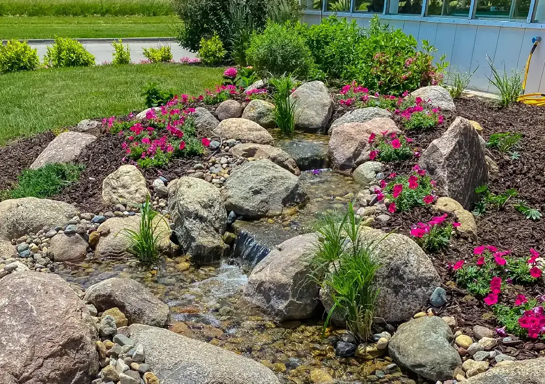 Pondless stream winding through boulders and pink flowering plants