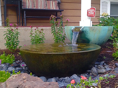 Single bowl fountain spilling into a stone basin in a front yard garden bed