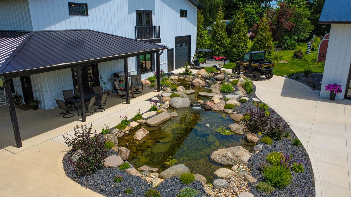 Long pond with a stream running beside a covered patio and concrete driveway