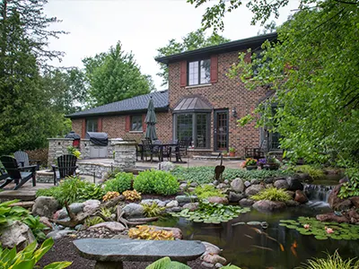 Large backyard pond with a biofalls filter behind a brick home and patio