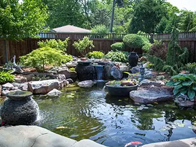 Large maintained pond with urn fountains and a waterfall along a wood fence
