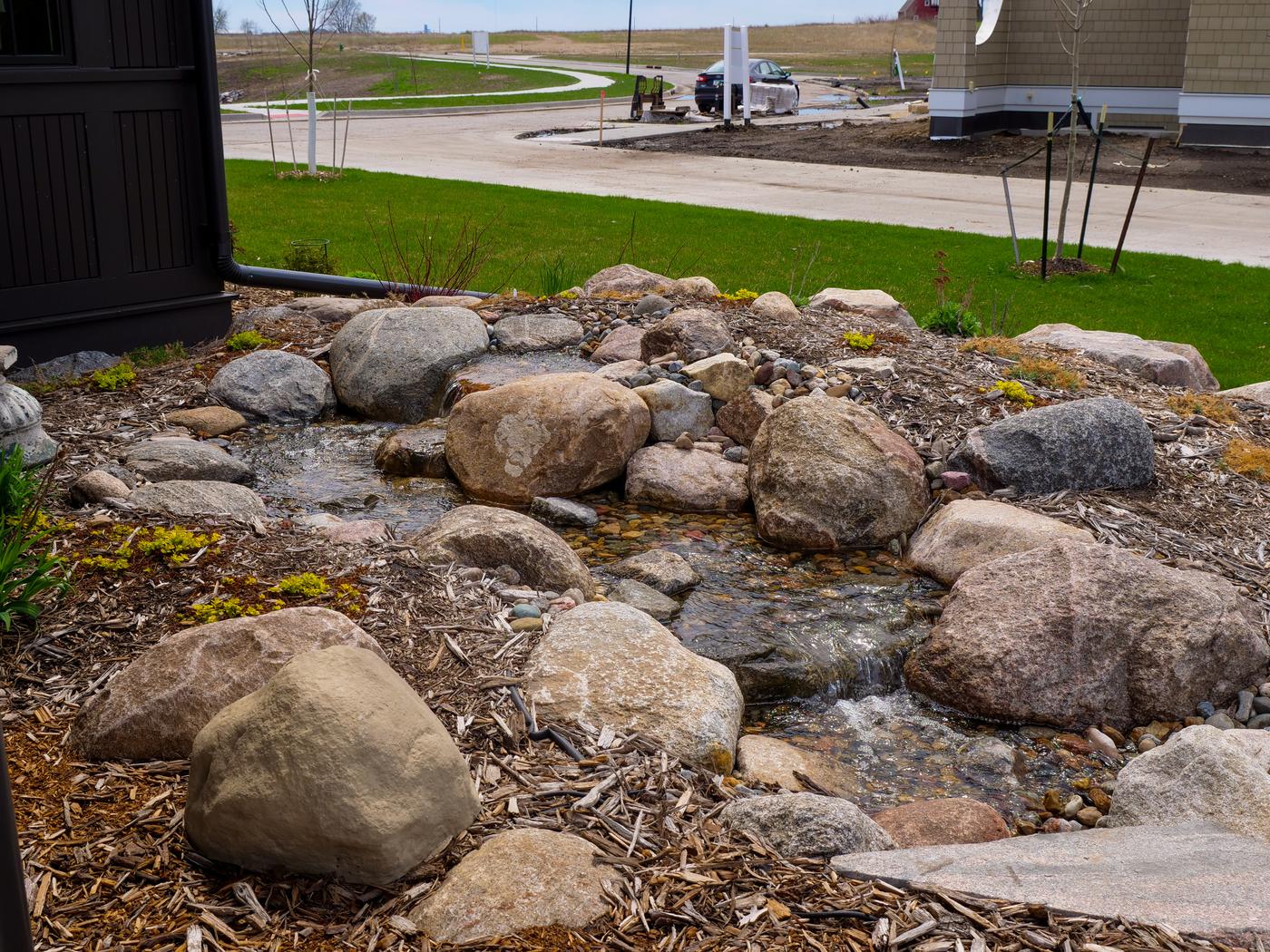 Small pondless stream tucked into a mulched bed beside a new home