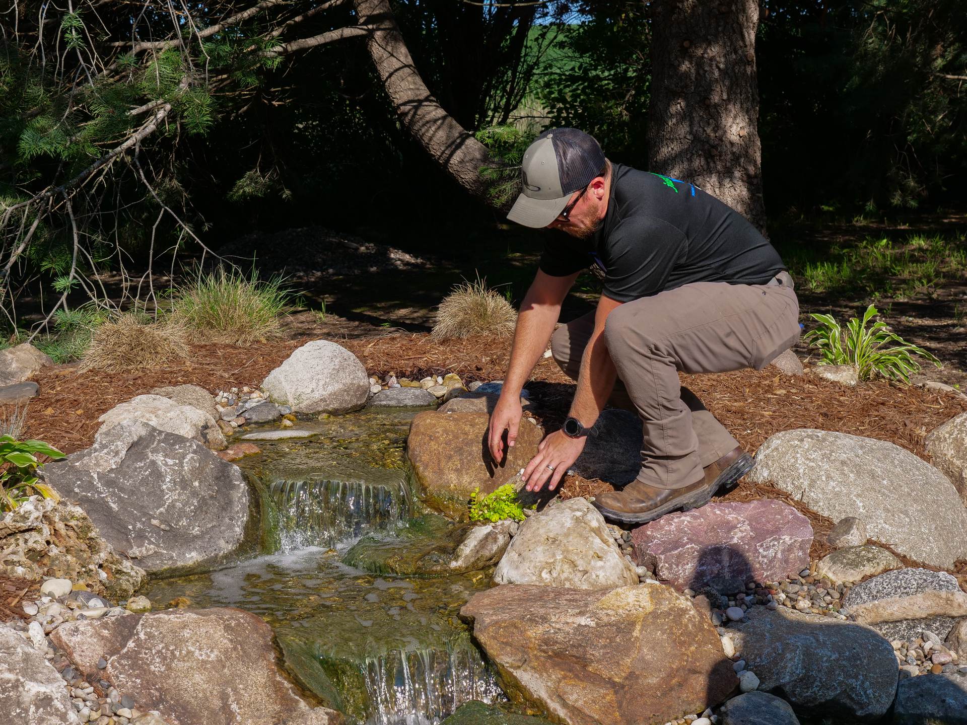 Just Add Water technician cleaning a pond edge beside a branded blue bucket