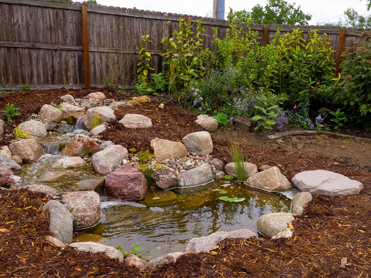 Small backyard pond with a short waterfall edged by boulders and mulch