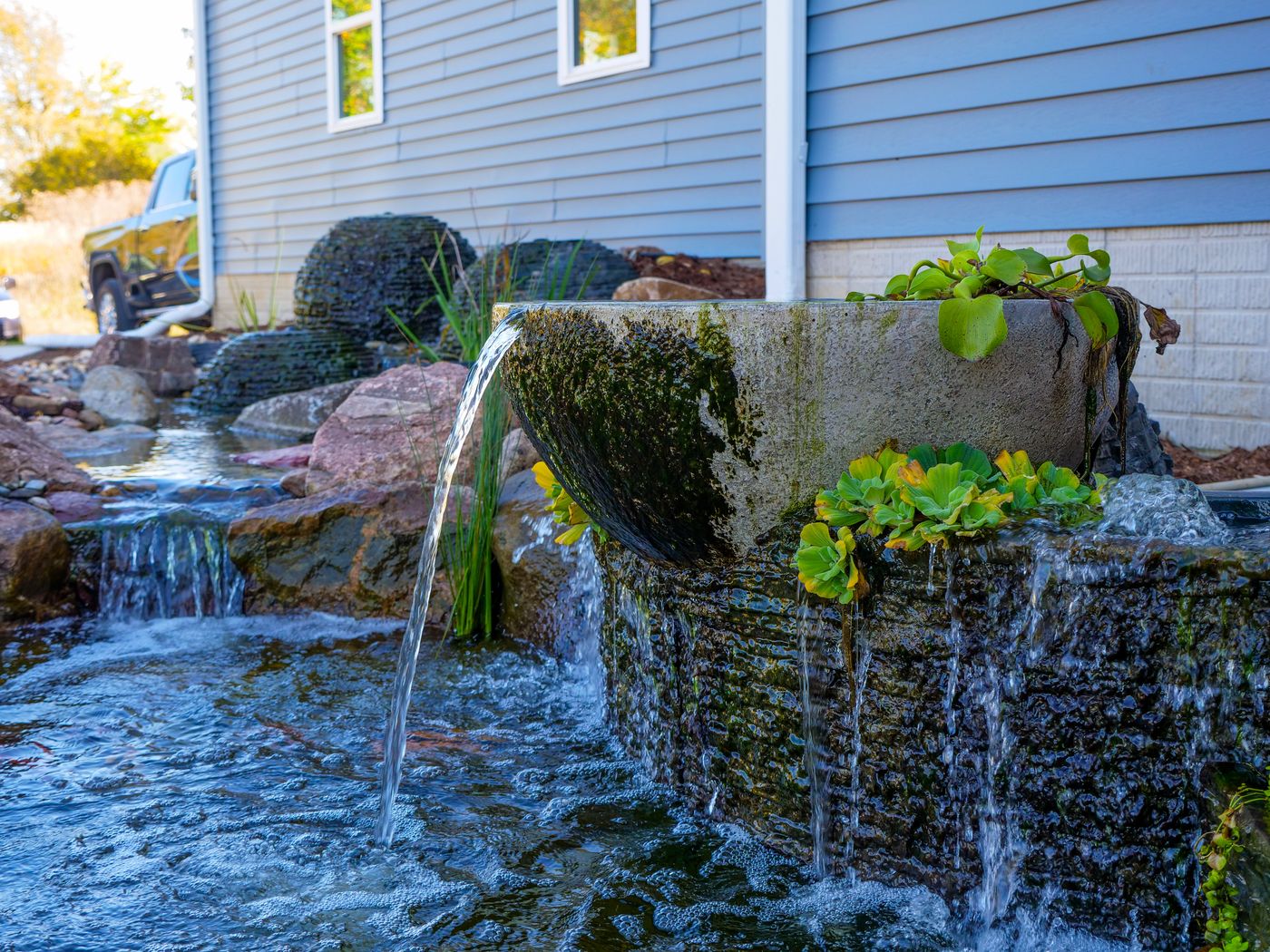 Stone bowl fountain pouring into a bubbling waterfall beside a home