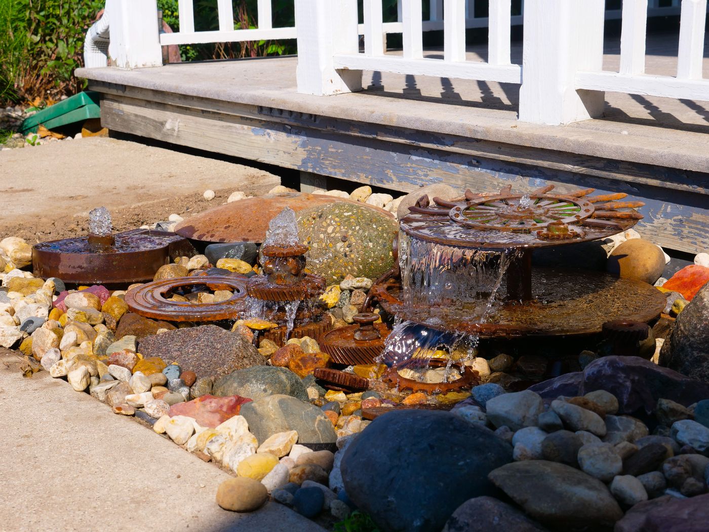 Whimsical fountain built from antique iron wheels and gears set in colorful river rock