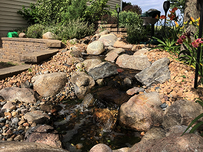 Pondless stream with four small waterfalls beside a stone retaining wall