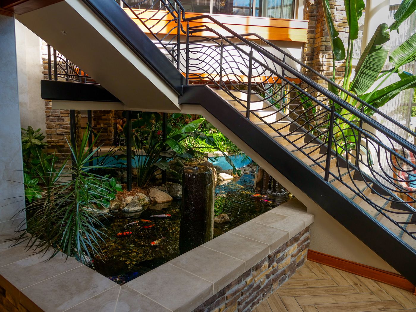Indoor pond with a stone spillway and tropical plants tucked beneath a staircase