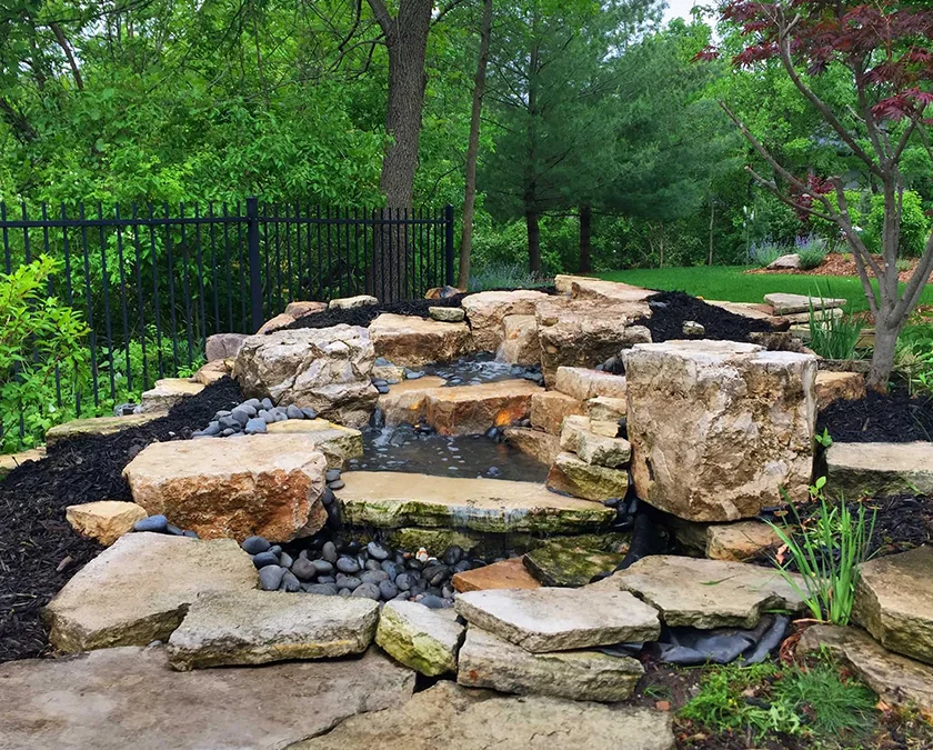 Repaired stream flowing over stacked limestone slabs in a fenced Des Moines backyard