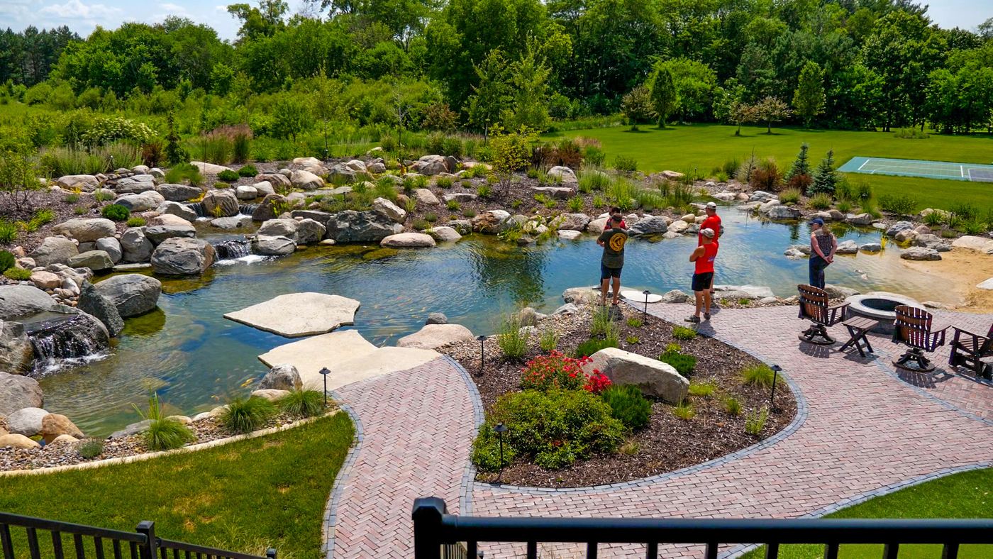 Large recreational pond with a paver path, fire pit seating, and a sandy entry