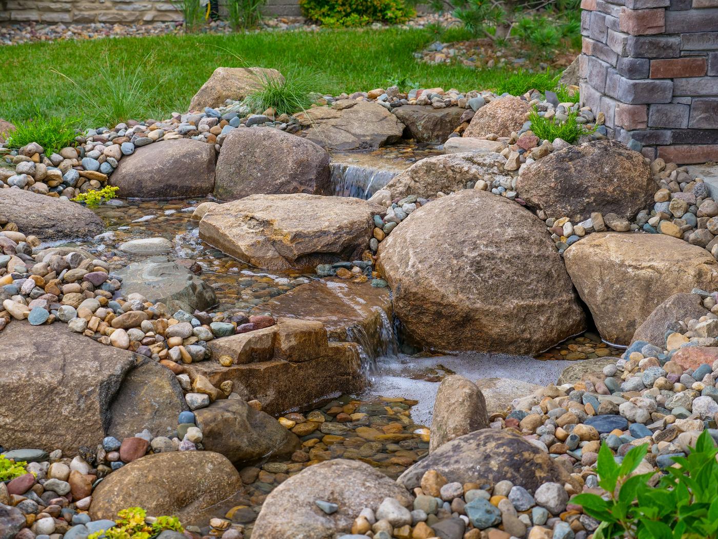 Pondless stream stepping over boulders alongside a stone house corner