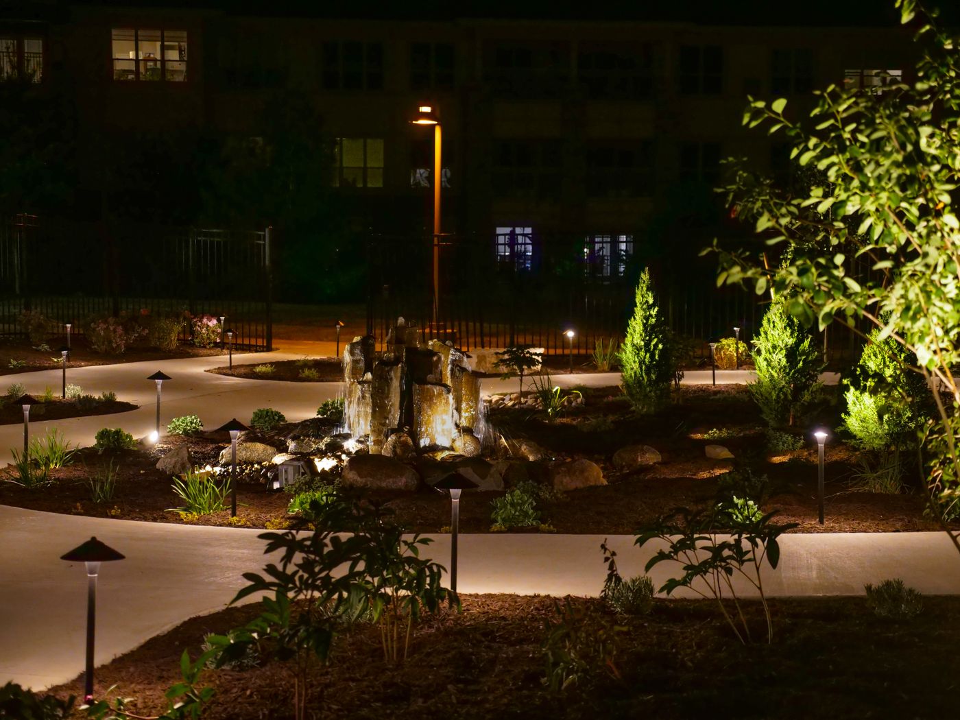 Lit basalt column fountain glowing in a landscaped courtyard at night