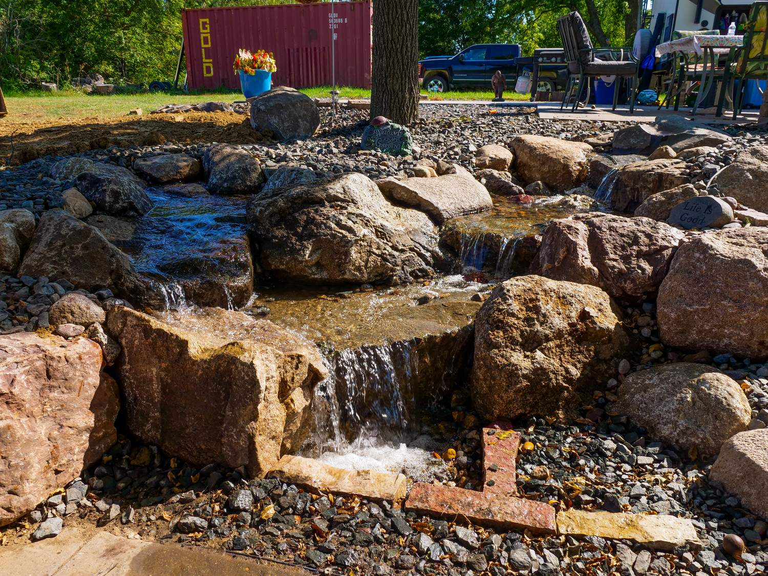 Pondless stream with small waterfalls running through boulders under a shade tree