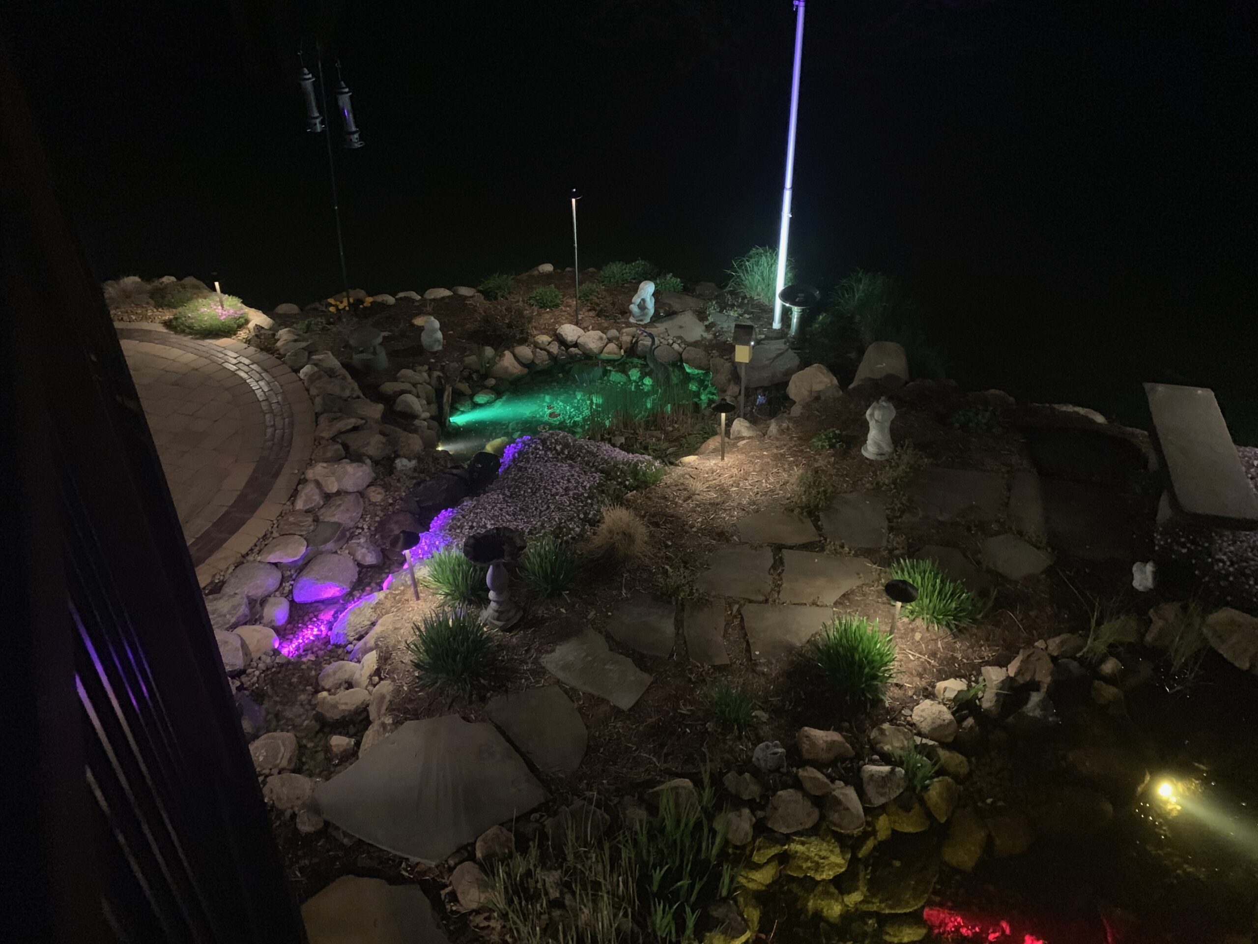 Night view from a deck of a lit waterfall, patio, and garden lights