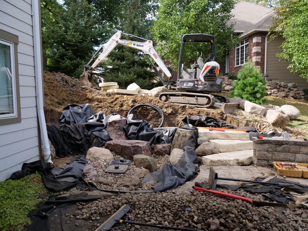 Excavator landscaping home backyard with rocks and dirt.